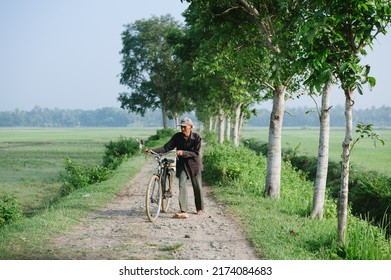 Kebumen, Indonesia - January, 2016: An Old Man Pushes A Bicycle On A Rocky Road.