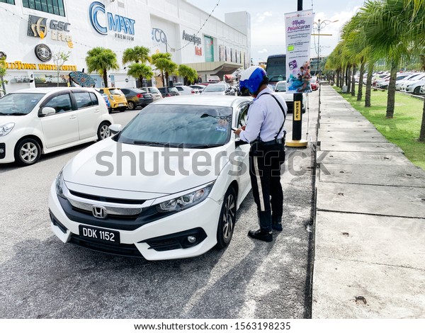 KEDAH,MALAYSIA-CIRCA\
NOVEMBER,2019 : Traffic police officer writing a traffic ticket to\
a car parked in a no parking\
area.