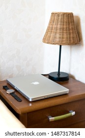 Kedainiai, Lithuania - August 25, 2019: Night Lamp, Macbook Pro And Wristwatch On The Night Stand Table In Bedroom. 