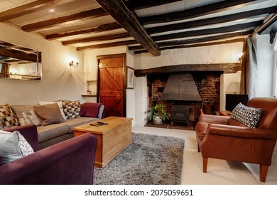 Kedington, Suffolk - November 19 2019: Furnished Traditional English cottage living room or lounge with exposed beams and fireplace with cast iron woodburning stove within exposed brick fireplace