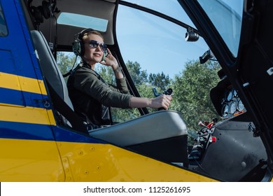 Keen on flying. Gorgeous young female pilot sitting in the pilot booth of a helicopter and posing for the camera while holding a steering wheel
