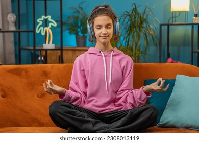 Keep calm down, relax. Preteen school girl breathes deeply with mudra gesture, eyes closed meditating with concentrated thoughts, peaceful mind. Young child kid at home room apartment sitting on couch - Powered by Shutterstock