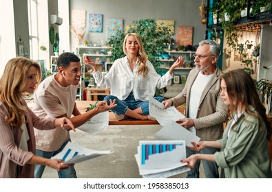 Keep calm and no stress! Young woman is sitting in lotus position while her colleagues are arguing nearby. Multiracial people working together in modern office.