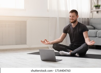 Keep calm on quarantine. Millennial guy meditating with trainer online via laptop connection, empty space