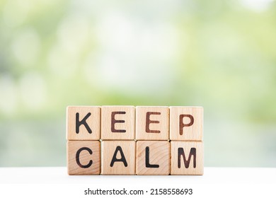 KEEP CALM - word is written on wooden cubes on a green summer background. Close-up of wooden elements.