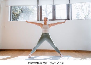 Keep fit, stay healthy. Beautiful mature woman doing her yoga strength training in living room while standing at warrior pose - Powered by Shutterstock