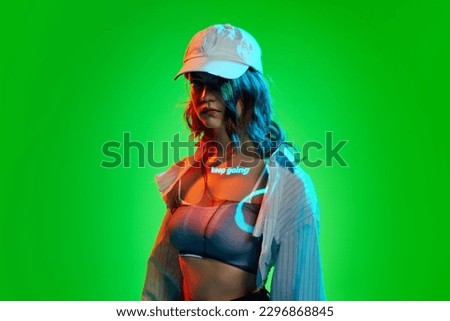 Keep going. Creative portrait of young girl wearing cap with digital neon filter lights with inscryption on body on bright green mode background. Concept of digital art, fashion, cyberpunk, futurism