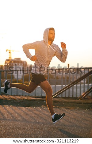 Keep on moving! Side view of confident young man looking forward while running along the bridge