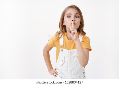 Keep Quiet Please. Determined Obedient Cute Blond Girl Child Showing Hush Sign, Shushing Asking Silence, Hold Finger On Lips Turn Off Loud Music, Sharing Secret, Stand White Background