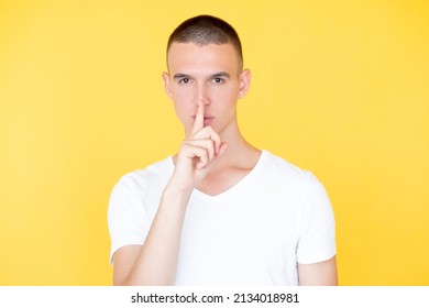 Keep Secret. Silent Man. Mute Expression. Serious Hipster Guy In Casual White T-shirt Holding Shush Finger On Mouth Isolated Yellow.