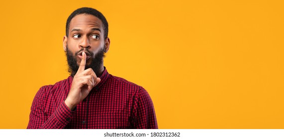 Keep Silence. Black Guy Making Hush Sign, Holding Finger On Lips, Looking Aside At Copy Space, Yellow Wall, Panorama