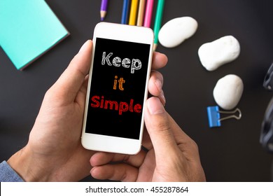 Keep it simple, text message on screen at hands take smartphone, black table with office supplies backdrop background . business concept.
