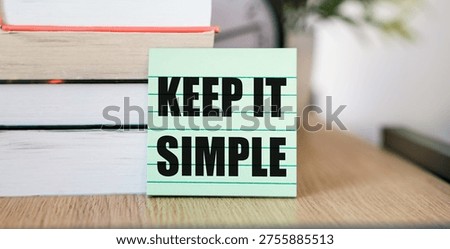 Keep It Simple text written on a green sticky note placed against a stack of books on a wooden desk. A conceptual image for minimalism, effective communication, uncomplicated lifestyle, and efficient problem-solving strategies.