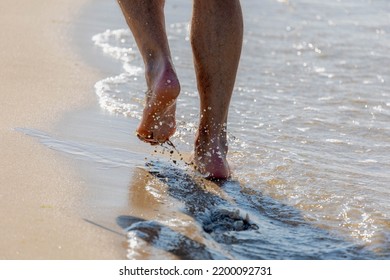 Keep Walking Concept, Selective Focus Of Bare Men's Feet With Approaching Seawave On The Shore, Low Angle Of Of A Man Walking On The Sand Beach With Footprints, Activities And Recreation In Summer.