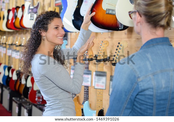 Keeper of musical instrument shop selecting\
guitar for customer