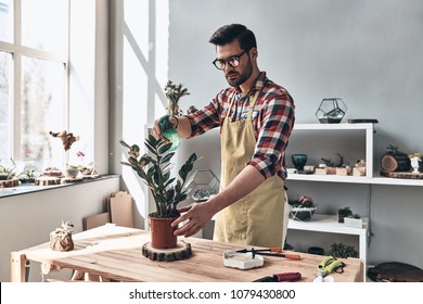 Keeping plants hydrated. Handsome young man in apron watering potted plant while standing in small garden center                     - Powered by Shutterstock