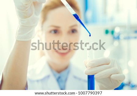 Keeping in a right proportion. Scaled up look on female lab worker holding a test tube and using a pipette while pouring blue chemical liquid during an experiment.