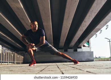 Keeping those muscles flexible. Handsome young African man in sports clothing stretching while warming up outdoors - Powered by Shutterstock