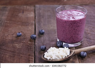 Kefir Grains In Wooden Spoon In Front Of Blueberry Kefir Smoothie. Kefir Is One Of The Top Health Foods Available Providing Powerful Probiotics.  