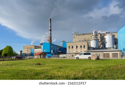 Kehra Estonia - May 28 2022:  Main industrial complex of pulp and paper mill belonging to Tolaram Group, Horizon Ltd. Tall chimney and historical brick building. Spring evening, green meadow in front.