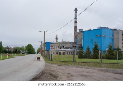 Kehra Estonia - May 28 2022:  Main industrial complex of pulp and paper mill belonging to Tolaram Group, Horizon Ltd. Tall chimney and historical building. Elderly lady walking on the street.