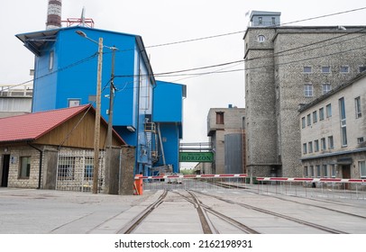 Kehra Estonia - May 28 2022:  Railroad leading to the main entrance of pulp and paper mill of Tolaram Group, Horizon Ltd. Blue industrial building in left, old brick house in right, barrier in front.