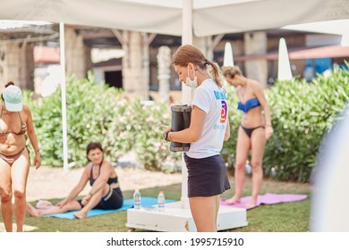 Kemer, Turkey - May 25, 2021: Fitness Trainer In Mask With Music Column Preparing For Morning Warm-up With Group. Outdoor Morning Exercises With A Fitness Trainer. Women Doing A Group Workout.