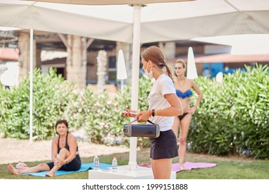 Kemer, Turkey - May 25, 2021: Fitness Trainer In Mask With Music Column Preparing For Morning Warm-up With Group. Outdoor Morning Exercises With A Fitness Trainer. Women Doing A Group Workout. 