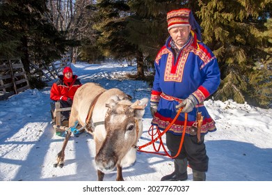 Kemi, Lapland, Finland - 2004: Reindeer Herder In Traditional Sami Costume, With Reindeer And Sled.