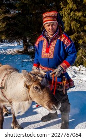 Kemi, Lapland, Finland - 2004: Reindeer Herder In Traditional Sami Costume, With Reindeer And Sled.