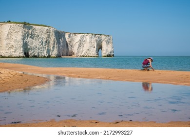 Kent, England - 14 June, 2022 - A a girl playing with sand on the beach at Kingsgate Bay in the seaside town of Broadstairs, with Kingsgate Bay Sea Arch in the background