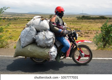 Kenyan Humble Man Riding His Bike On The Highway With An Excessive Amount Of Luggage On His Back.