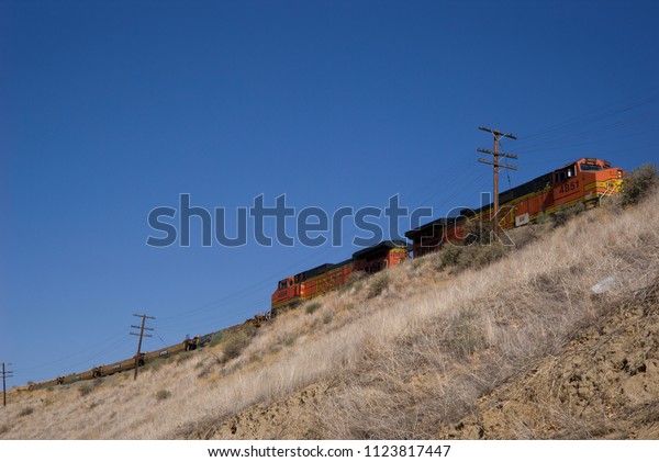 KERN COUNTY, CA -\
JUNE 26, 2018:  Diesel-electric locomotives strain against gravity\
as they haul their loaded train through the foothills of the Sierra\
Nevada Range.