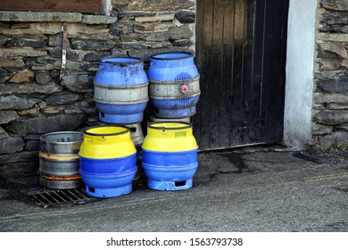 Keswick, Cumbria, UK - April 6th 2019: Blue And Yellow Beer Kegs Stacked Up Against A Stone Wall Outside A Pub In England