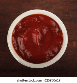 Ketchup In Cup On Wooden Background