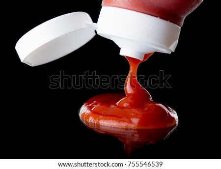 Ketchup or tomato sauce falling from bottle over dark background