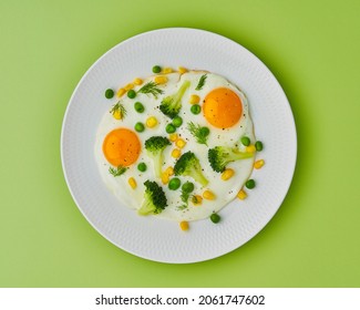 Keto balanced diet food. Fried eggs, broccoli, corn, peas, dill, pepper on white plate on green background. Cooking from leftovers. Horizontal, above