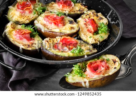 Keto diet dish: Avocado Boats with crunchy bacon, melted cheese and cress sprouts on dark background