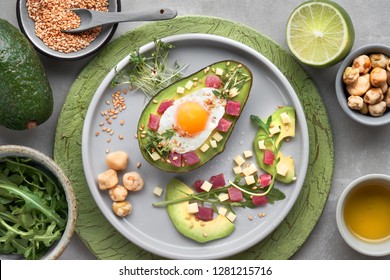 Keto Diet Dish: Baked Avocado Boat With Ham Cubes, Quail Egg And Cheese Served With Green Rucola Salad, Flat Lay On Grey Stone With Ingredients