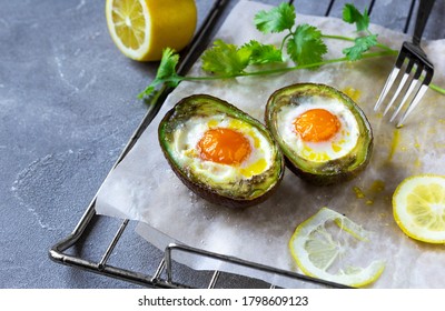 Keto Diet Dish: Baked Avocado Boats With Eggs, Lemon And Cilantro On Baking Paper On Grey Background