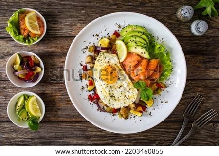 Keto diet - smoked salmon, sunny side up egg, avocado and mix of vegetables on wooden table 
