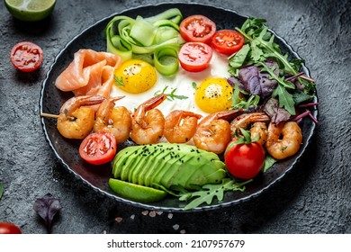 Ketogenic breakfast. Keto low carb salmon, grilled shrimps, prawns, fried eggs, fresh salad, tomatoes, cucumbers and avocado. keto diet. Top view.