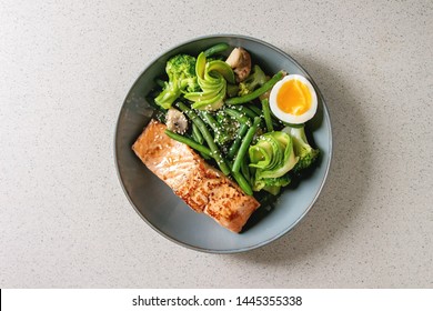 Ketogenic low carb diet dinner grilled salmon, avocado, broccoli, green bean and soft boiled egg in ceramic bowl over grey spotted background. Flat lay, space