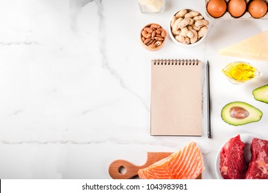 Ketogenic low carbs diet concept. Healthy balanced food with high content of healthy fats. Diet for the heart and blood vessels. Organic ingredients, white background, copy space top view, notepad 