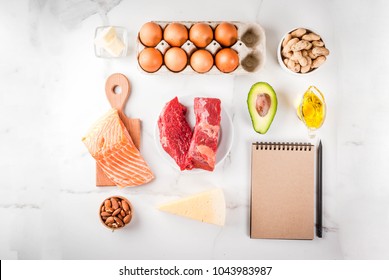 Ketogenic low carbs diet concept. Healthy balanced food with high content of healthy fats. Diet for the heart and blood vessels. Organic ingredients, white background, copy space top view, notepad 