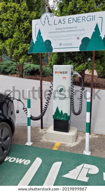 Ketrzyn, Poland - July 19, 2021 Hitler\'s Wolf\'s Lair\
Headquarters. A static shot of a solid black Tesla Model 3 dual\
motor long range charging at the POWER EV AC charging station in a\
sunny summer day