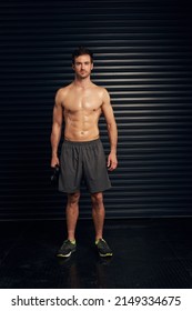 Kettle bells keep me in shape. Studio portrait of a shirtless and well built man standing against a dark background.