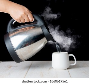 kettle pouring boiling water into a cup with smoke on wood table - Powered by Shutterstock