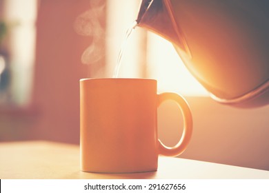 kettle pouring boiling water into a cup in morning sunlight