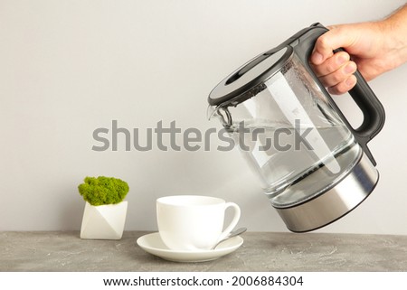 Kettle pouring boiling water into a cup on grey background. Top view.